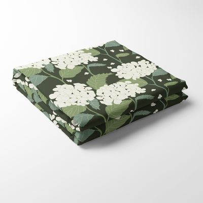En vikt bordsduk i mönstret Hortensia Grön med vita hortensiablommor och gröna blad mot en mörkgrön bakgrund.