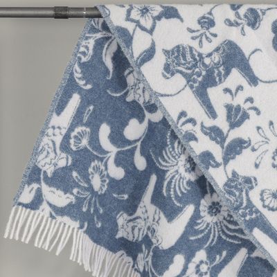 Närbild av ullpläd med dalahästar och blommönster i blått