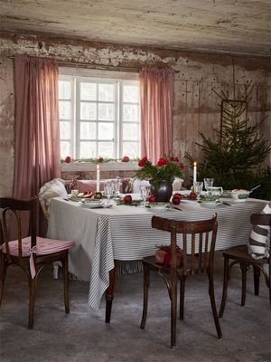 Juldukning i lantligt kök med Anna röd randiga gardiner, trästolar, gran och tända ljus – klassisk svensk julstämning.