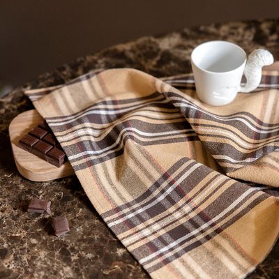 Ecossais beige draperat över en bänk med kopp och choklad, med rutmönster i beige, brunt, naturvitt och rött.