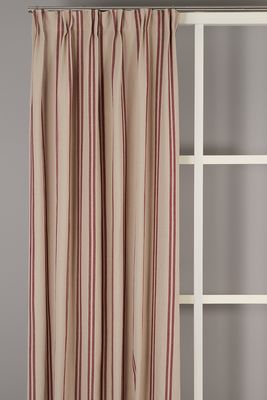 Hedvig beige gardin med broderade röda ränder som hänger i mjuka veck vid ett fönster.