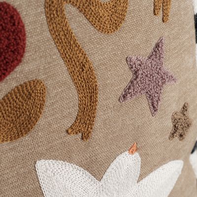 Detaljbild av Kuddfodral Paloma med broderad stjärna, blomma och dekorativa former som visar broderiets struktur mot den beige botten.