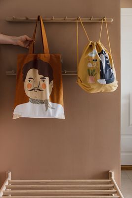 Rostfärgad tygkasse med Carlos-motiv som hänger på träkrokar