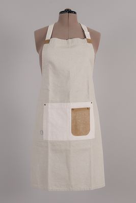 Beige förkläde med stor vit ficka och brun läderdetalj på fickan, fotograferat framifrån.