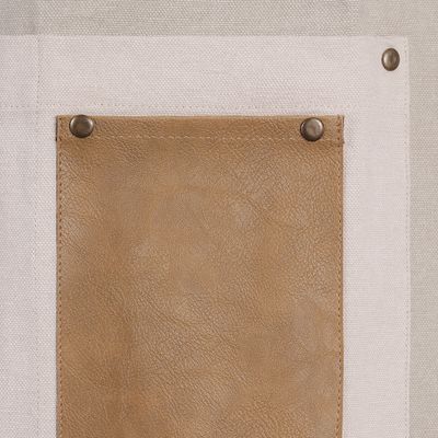 Närbild på vit ficka med brun läderficka och metallnitar på beige förkläde.