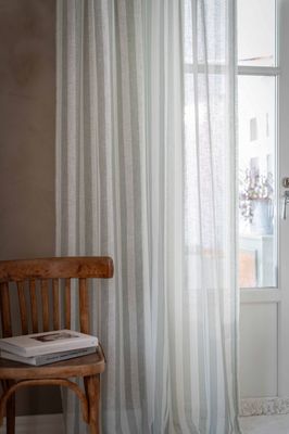 Disa gardin i ljusgrönt upphängd vid ett fönster i ett rum med trästol och naturligt ljusinsläpp.