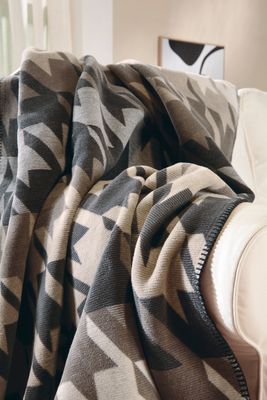 Mjuk filt med grafiskt mönster draperad över ljus soffa.