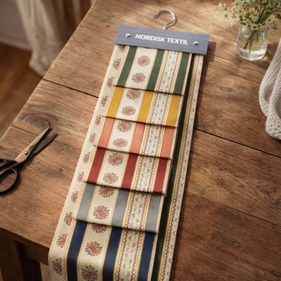 Tygprov av Bianca randigt stiltyg i röd nyans upphängt på provhängare i inomhusmiljö