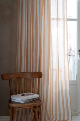 Disa gardin i gult och vitt i ett luftigt rum med trästol vid fönster