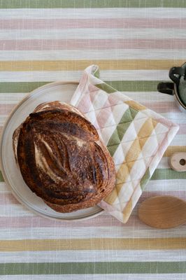 Närbild av Alba randig bordsduk i rosa, grönt och gult med bröd på tallrik och matchande kökshandduk.