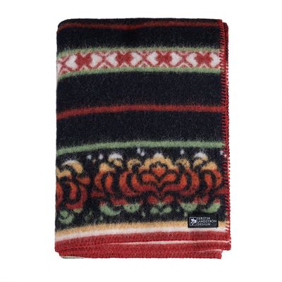 Kerstin Landström Design Bunad ullfilt i svart med traditionellt folkloristiskt mönster i rött, grönt och vitt, vikt mot ljus bakgrund.