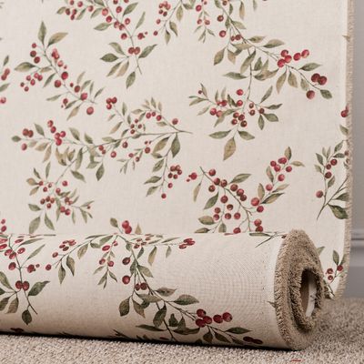 Jakobsdals Berra beige fotograferat på rulle framför ett upphängt tygstycke, med spridda lingonkvistar och den naturligt melerade beige väven väl synlig.