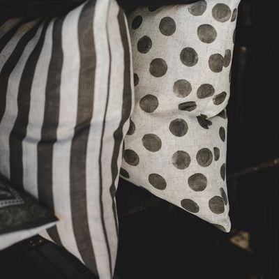 Grönrandigt kuddfodral tillsammans med prickig kudde i naturtoner i mörk inredningsmiljö.