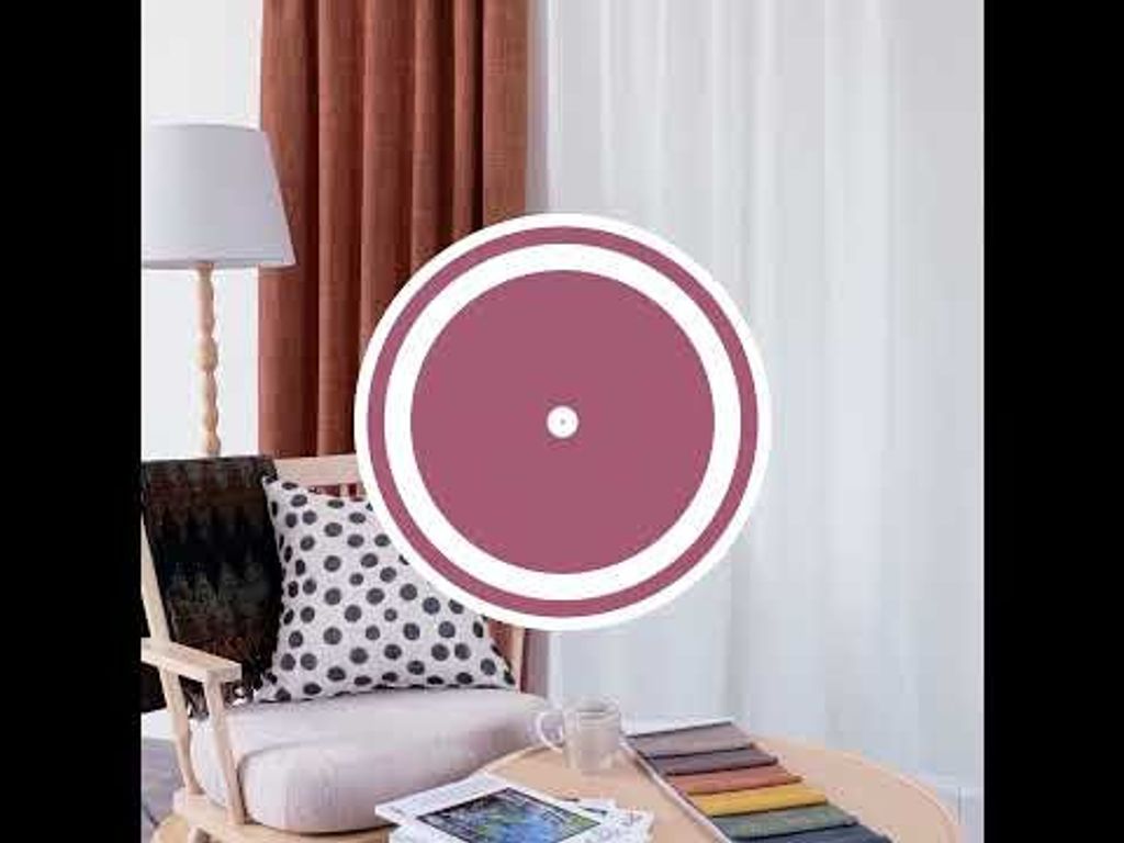 Video med långsam panorering i vardagsrumsmiljö med Cru rost mörkläggningsgardin, ljus träfåtölj med prickig kudde, pläd, kaffekopp med lätt ånga och tygprover på runt bord.