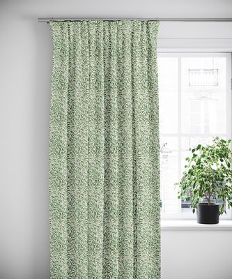 Ester grön gardin upphängd vid ett vitt fönster, tillsammans med grön växt i svart kruka.