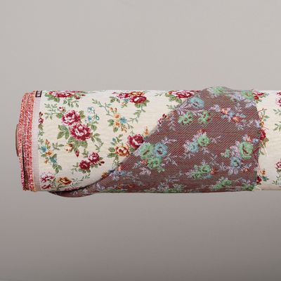 Närbild på hoprullat Nina beige jacquardvävt möbeltyg där både det romantiska rosmönstret på framsidan och den invävda baksidan syns.