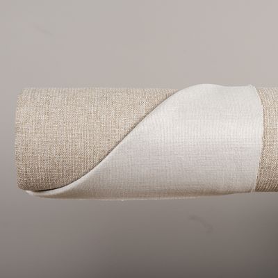 Möbeltyget Coco beige sand från Safeco på rulle med baksidan uppvikt för att visa både den vävda framsidan och den ljusa baksidan.