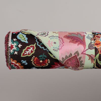 Närbild på hoprullat Shaman svart möbeltyg där både det färgstarka jacquardvävda blommönstret och tygets ljusare baksida syns.