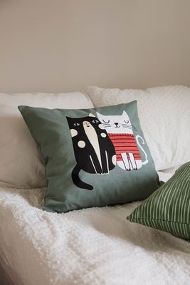 Kuddfodral med motiv av två katter, Sally och Doris, placerat i en ljus soffa tillsammans med andra kuddar