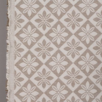 Detaljbild av Wilma beige bolstertyg som visar tygets vävda struktur, blommönster och fransade stadkant.