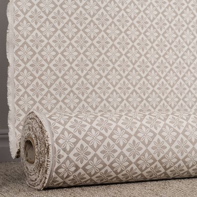 Wilma beige bolstertyg på rulle med återkommande blommor och romber i beige och naturvita toner.