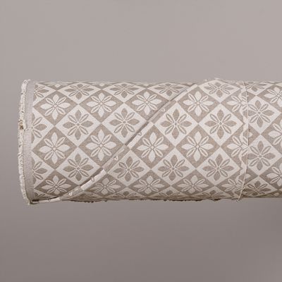 Närbild på rullat Wilma beige bolstertyg där det vävda blommönstret och tygets båda sidor syns.