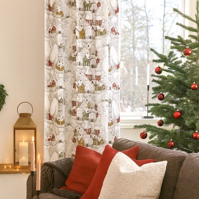 Vardagsrum dekorerat för jul med gardinen Snöskimmer, julgran och röda kuddar i soffan.