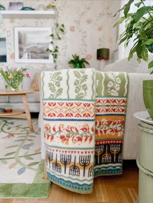 Kustland ullfilt draperad över en fåtölj i ett ljust vardagsrum med gröna och blommiga detaljer.