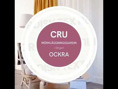 Video med långsam panorering över vardagsrumsmiljö med Cru ockra mörkläggningsgardin, fåtölj med rostfärgad kudde, kaffekopp med lätt ånga och tygprover på runt bord.