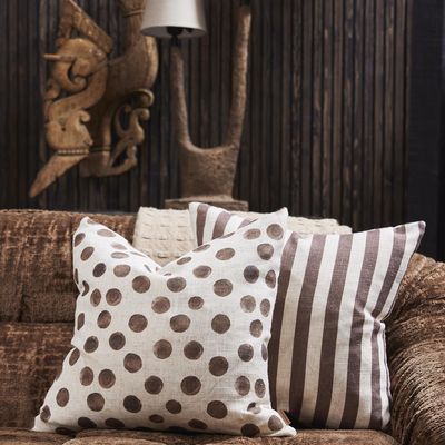 Brunrandigt kuddfodral tillsammans med prickig kudde i bruna toner på brun soffa.