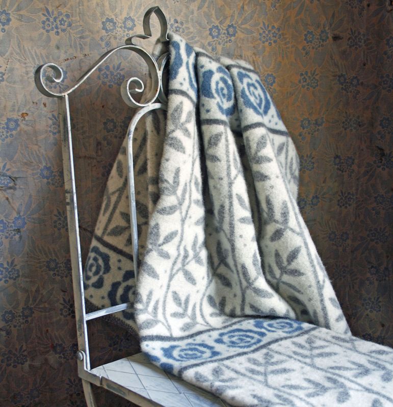 Ullfilten 'Rosengård' draperad över en vit järnstol, visar sitt klassiska rosmönster, perfekt för att addera en touch av elegans till varje rum.