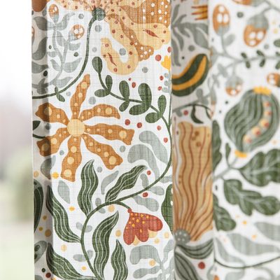 Närbild av Myllra gardin som visar detaljer i mönstret: blommor, blad, fröställningar och slingrande växter i varma toner.