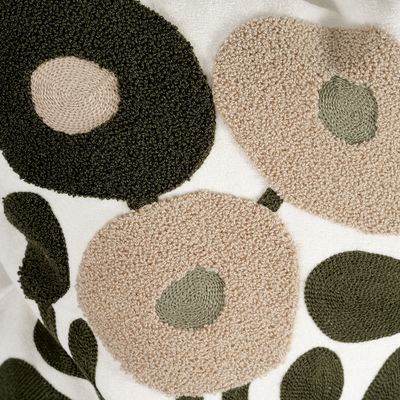 Närbild av Sabina kuddfodral som visar broderade blommor i beige och gröna nyanser med struktur från olika brodyrtekniker.