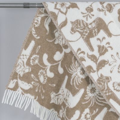 Närbild av ullpläd med dalahästar och blomdetaljer i beige toner