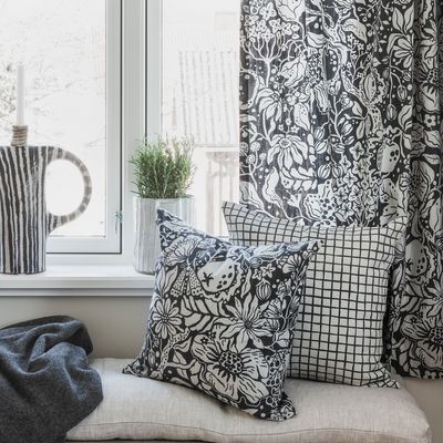 Kuddfodral Äppelpäppel asfalt från Spira of Sweden i en fönsternisch, stylat med andra svartvita mönster och växter i bakgrunden.
