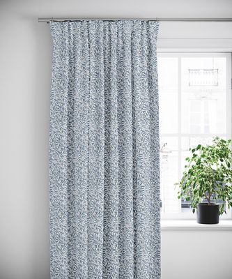 Duvblå gardin i botaniskt mönster framför ljust fönster med blomkruka
