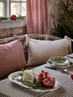 Röd- och vitrandig gardin Anna från Nordisk Textil, stylad med matchande kuddfodral i lantlig miljö med rustik trävägg.