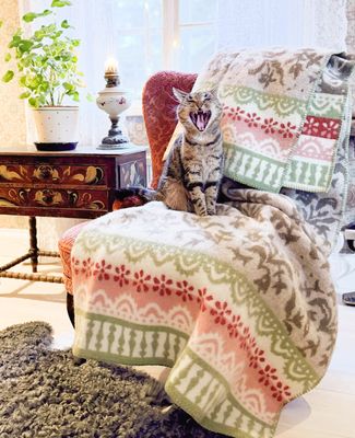 Torpet ullfilt över fåtölj i ljus lantlig miljö, med katt som sitter på filten och skapar en hemtrevlig atmosfär.