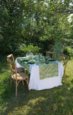 Dukning utomhus med Vildblommor bordslöpare på vitt bord, omgiven av grönska