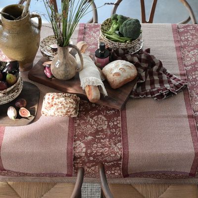 Vinröd bordduk med beige blommönster, använd på ett dukat bord med rustik känsla.